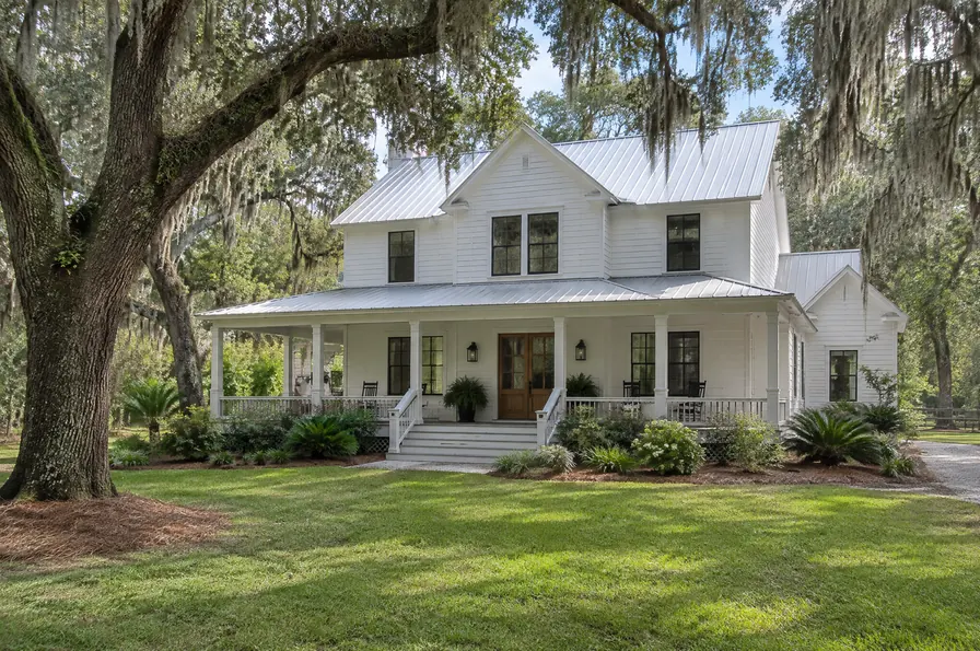 Two-story farmhouse with a wide front porch under live oaks